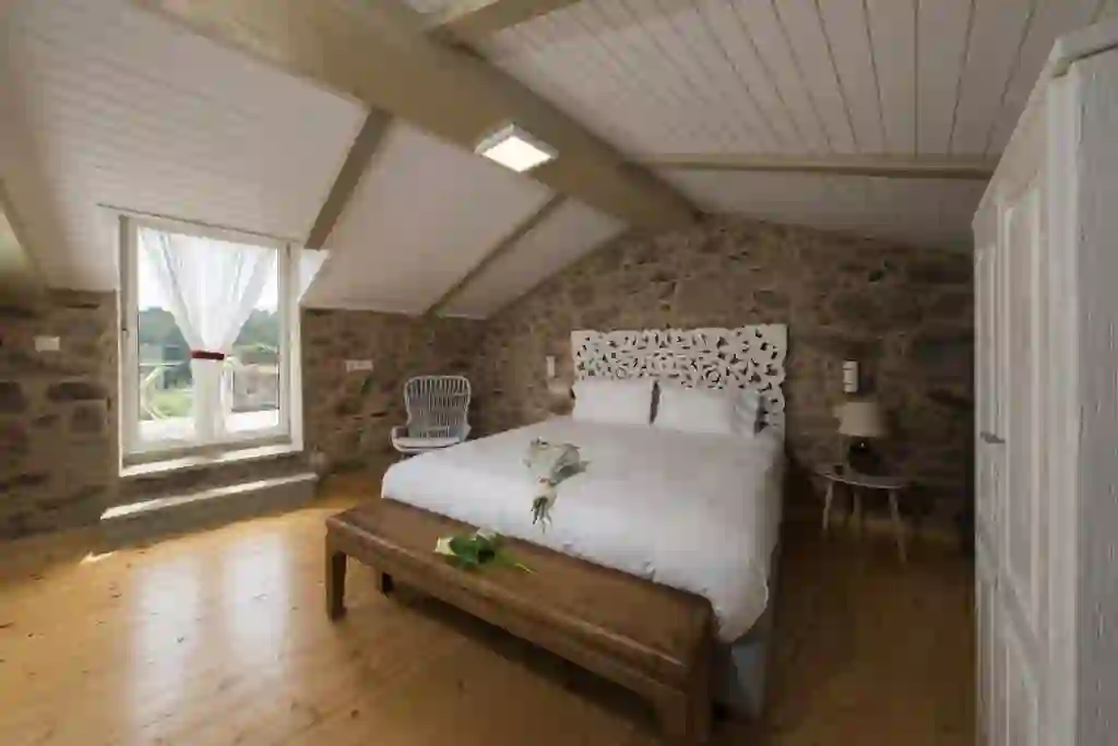 Dormitorio abuhardillado en piedra con cabecero tallado, Cabaña de Nemiña