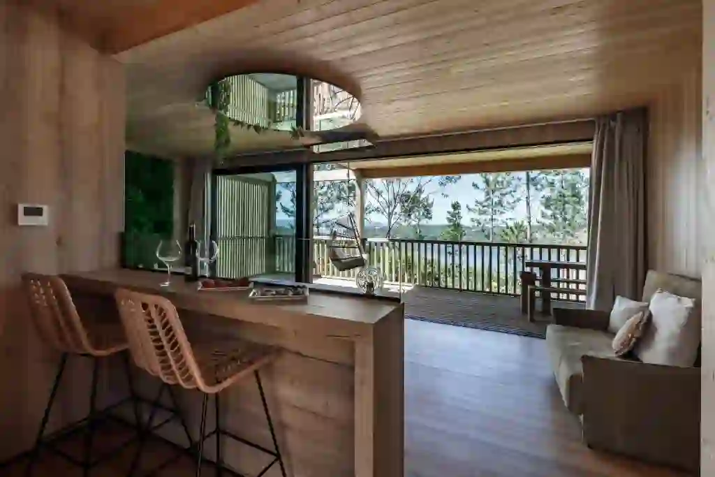 Zona de estar y cocina abierta con barra de madera y vistas a la ría, Cabanas da Luz