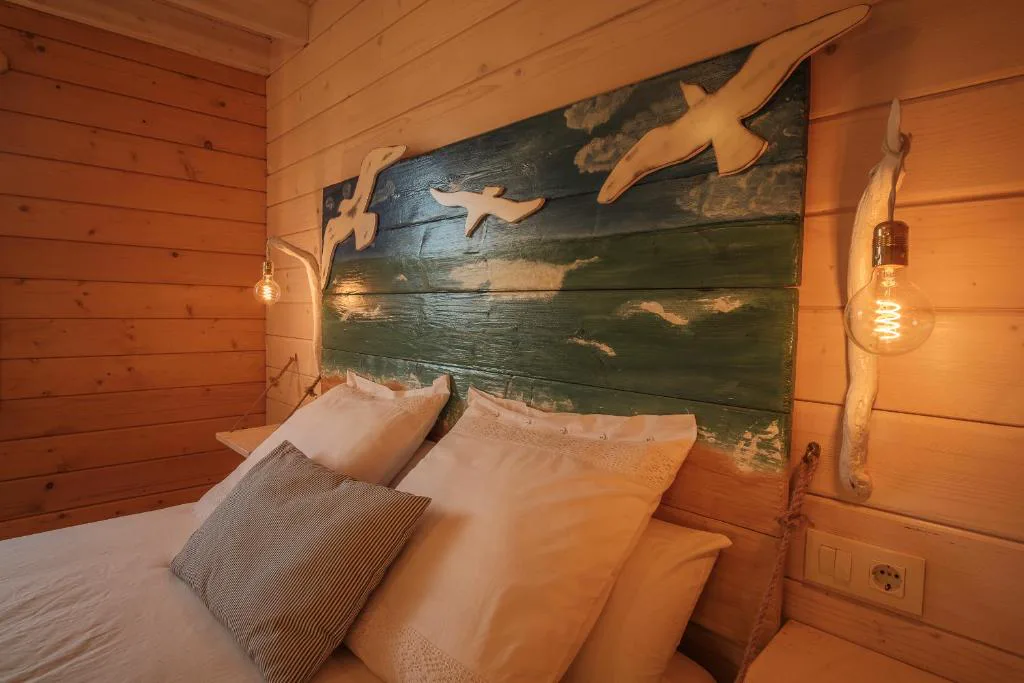 Cabecero de madera pintado con gaviotas sobre cama con cojines blancos, Cabanas da Ría