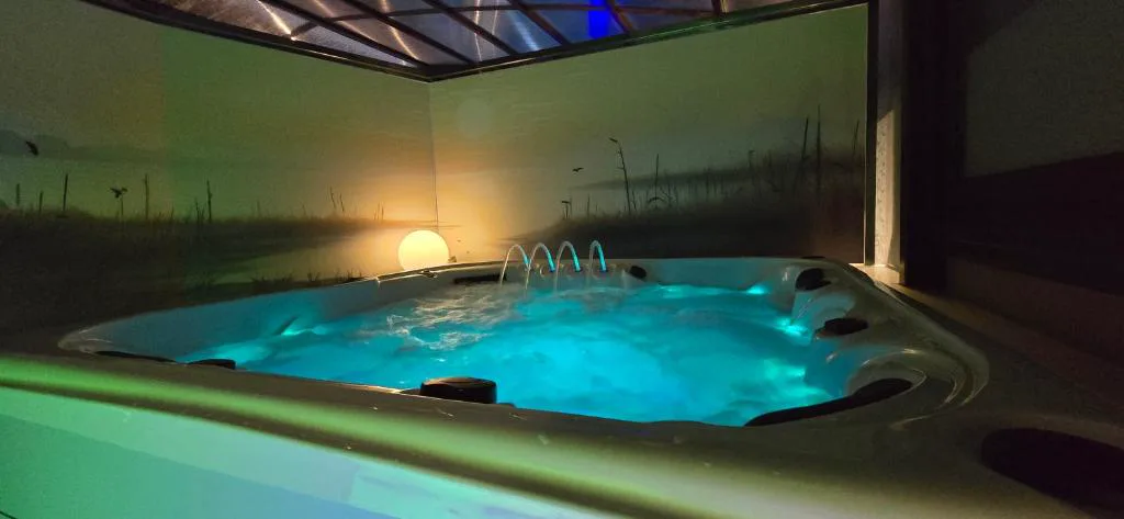 Bañera de hidromasaje interior con iluminación turquesa y mural de atardecer, Cabanas da Ría