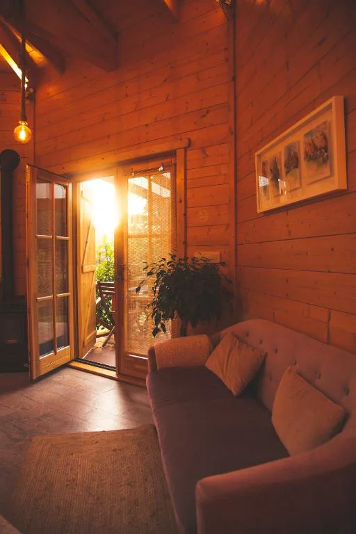 Salón con estufa de leña y sofá junto a puerta de madera abierta al jardín, Cabanas da Ría