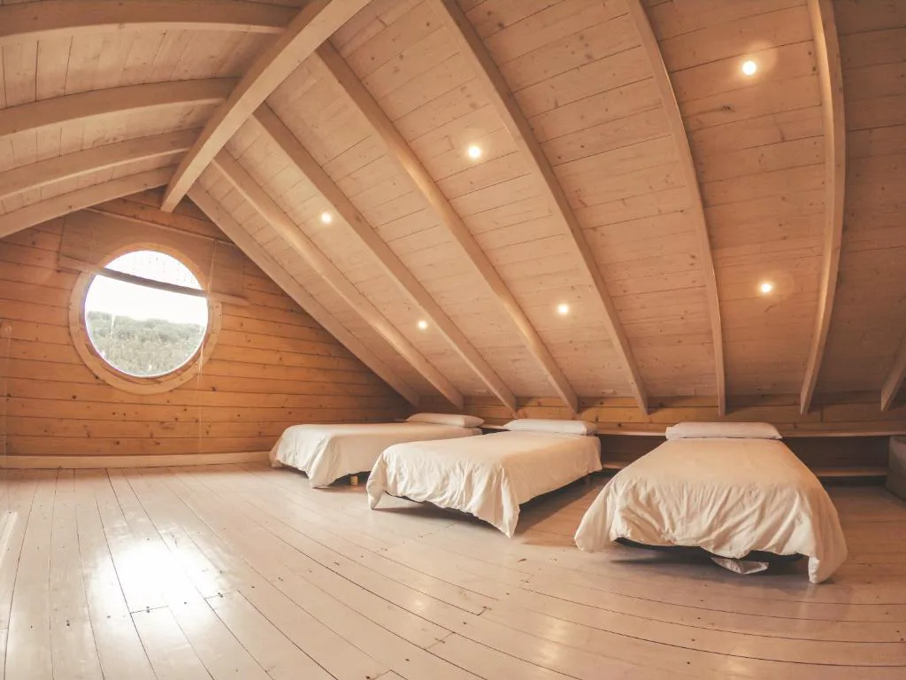 Interior de cabaña con techo de madera curvo en forma de casco de barco y ojo de buey, Cabanas da Ría