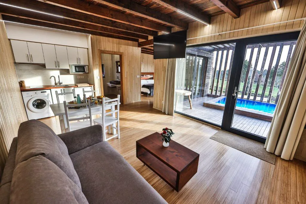 Salón con cocina abierta y vistas directas a la piscina a través de los ventanales, Cabañas de Mallas