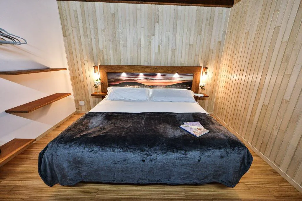 Dormitorio de madera con cabecero iluminado y manta gris, Cabañas de Mallas