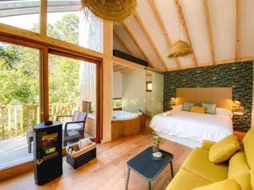 Dormitorio abuhardillado con jacuzzi de piedra, cama y sofá amarillo mostaza, Cabañas de Udra en Bueu