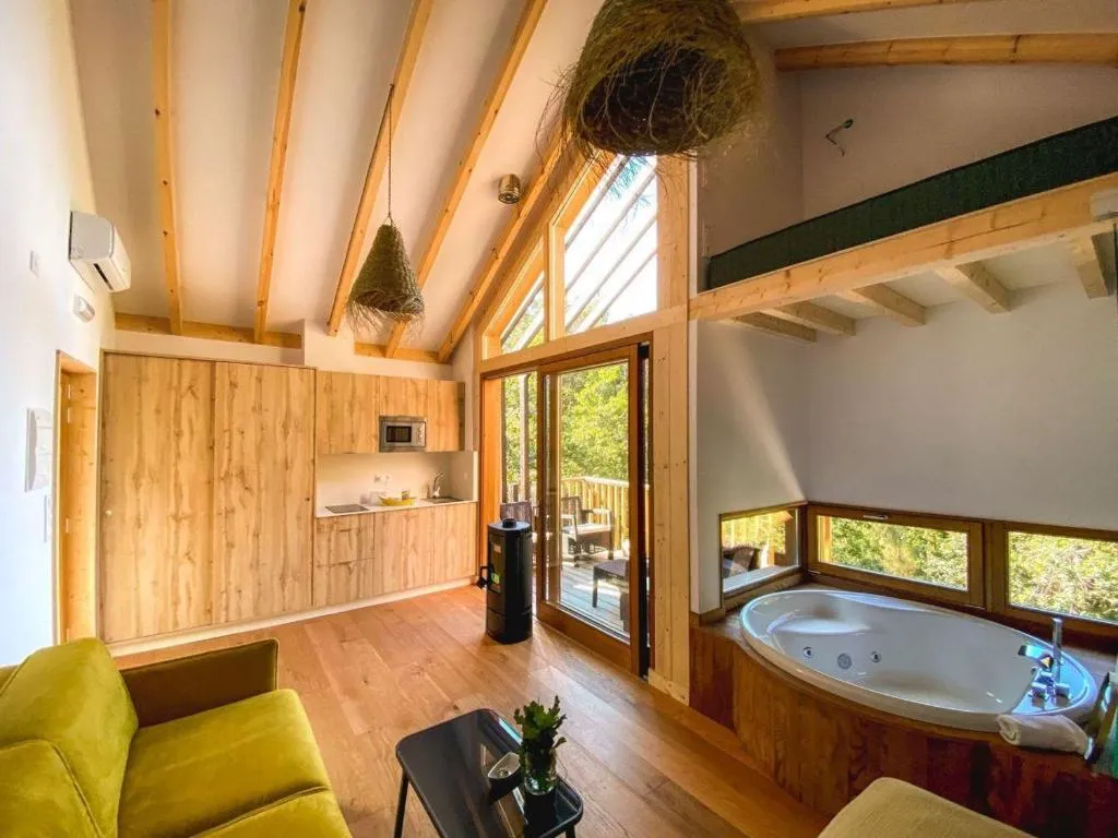 Salón con techos a dos aguas, cocina de madera y jacuzzi junto al ventanal, Cabañas de Udra