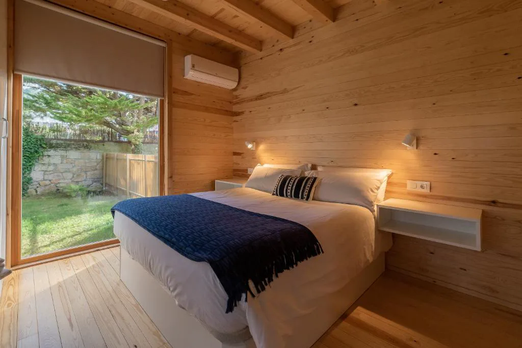 Dormitorio de madera con manta azul y ventanal corredero al jardín, Cabanas Narea