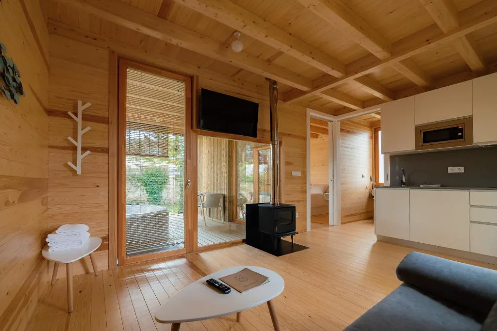 Salón con estufa de leña, cocina abierta y vistas a la bañera de hidromasaje exterior, Cabanas Narea