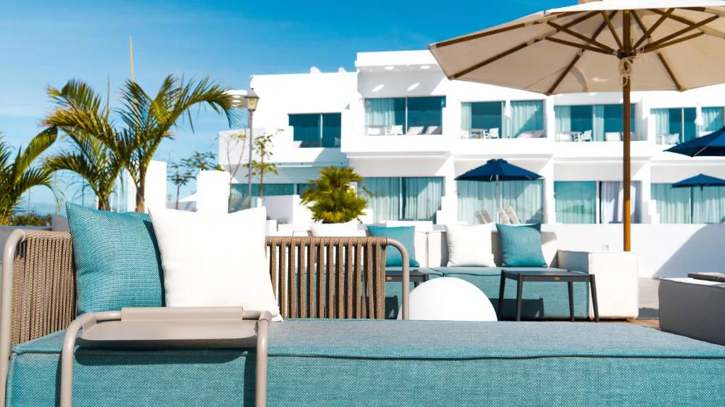 Terraza chill-out con cojines turquesa frente a la fachada blanca del hotel, CalaLanzarote Suites Hotel