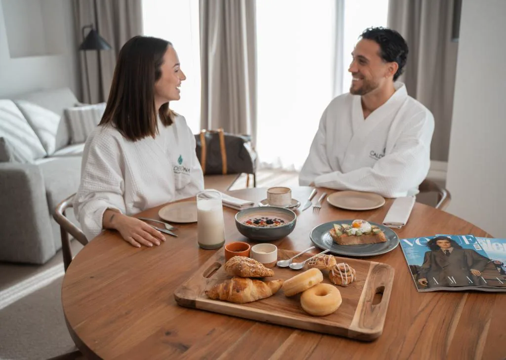 Pareja en albornoz desayunando en una mesa de madera