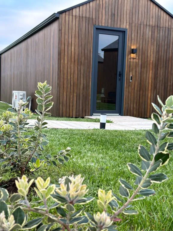 Fachada de madera de una cabaña con jardín y planta ornamental en primer plano, Camiño do Mar