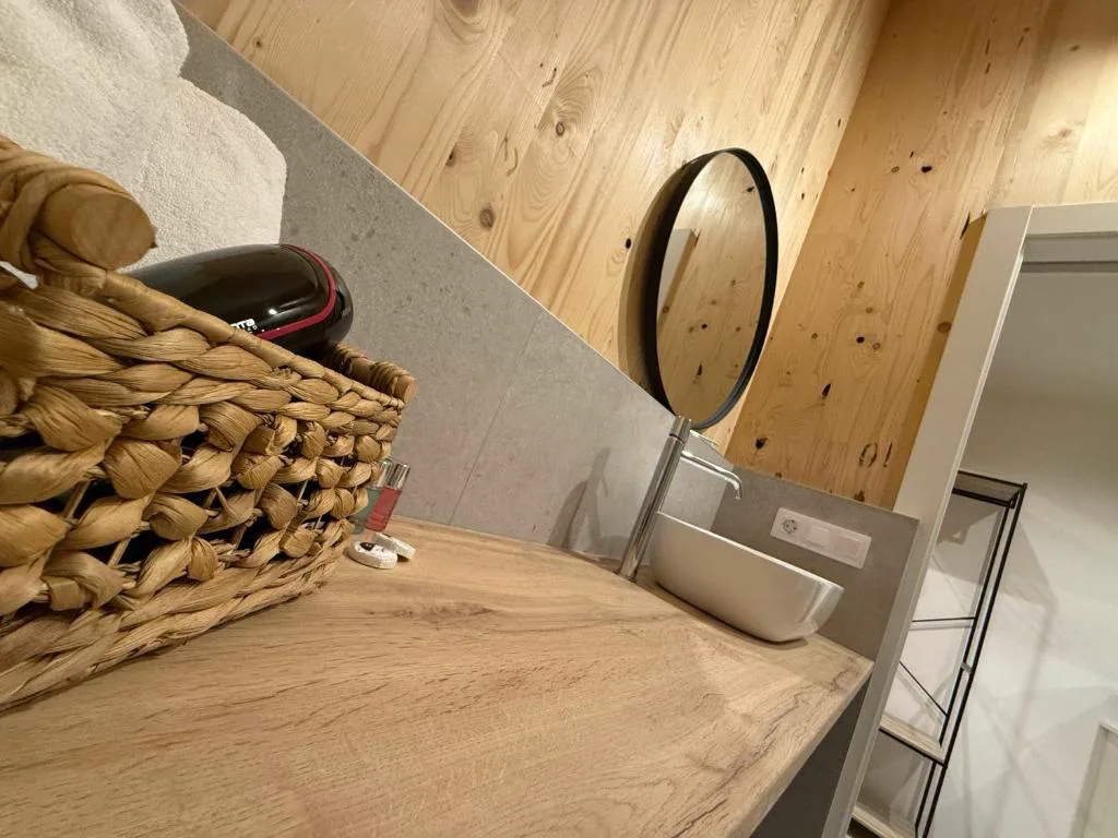 Detalle de lavabo con espejo redondo y cesta de mimbre con amenities, Camiño do Mar