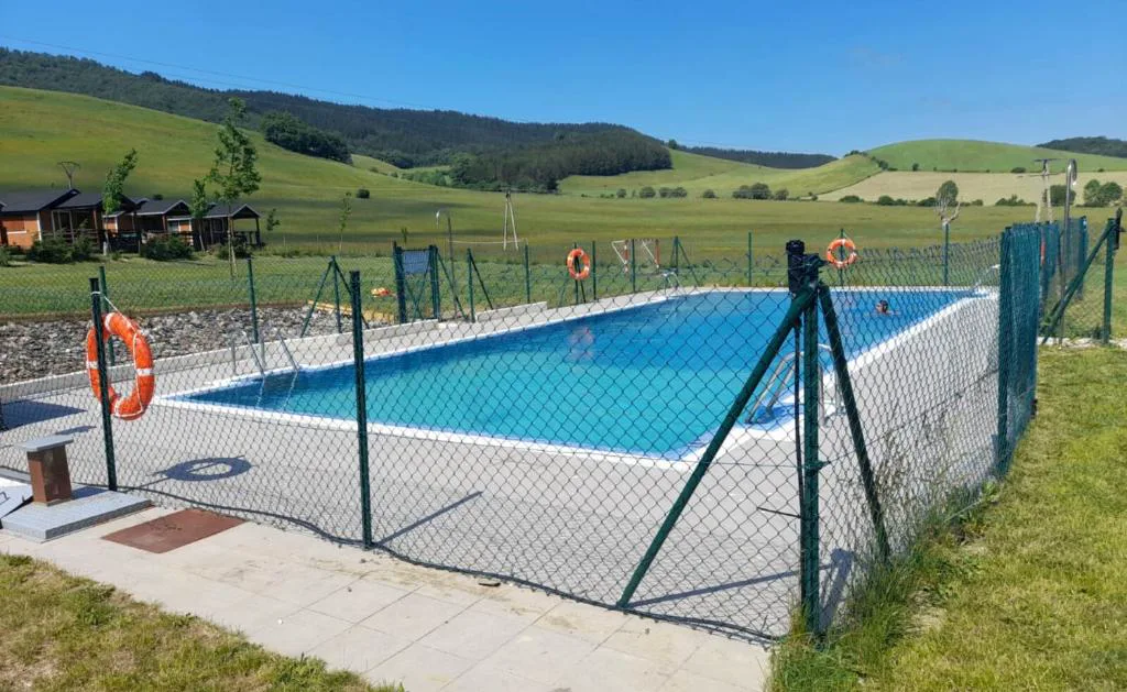 Piscina rectangular vallada con praderas y caravanas al fondo