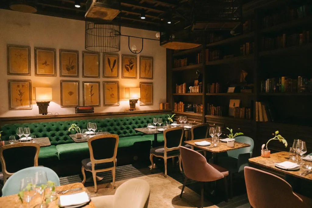 Restaurante con sofá de terciopelo verde y estanterías de libros antiguos, Can Bordoy Grand House
