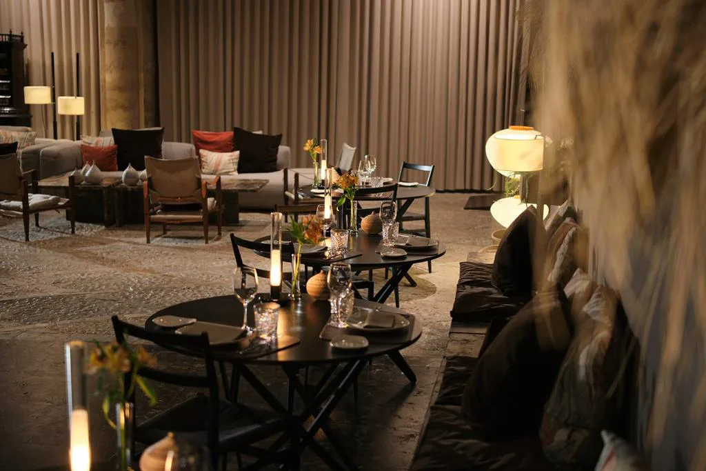 Restaurante con mesas redondas y velas encendidas junto a cojines de suelo, Can Cera Hotel