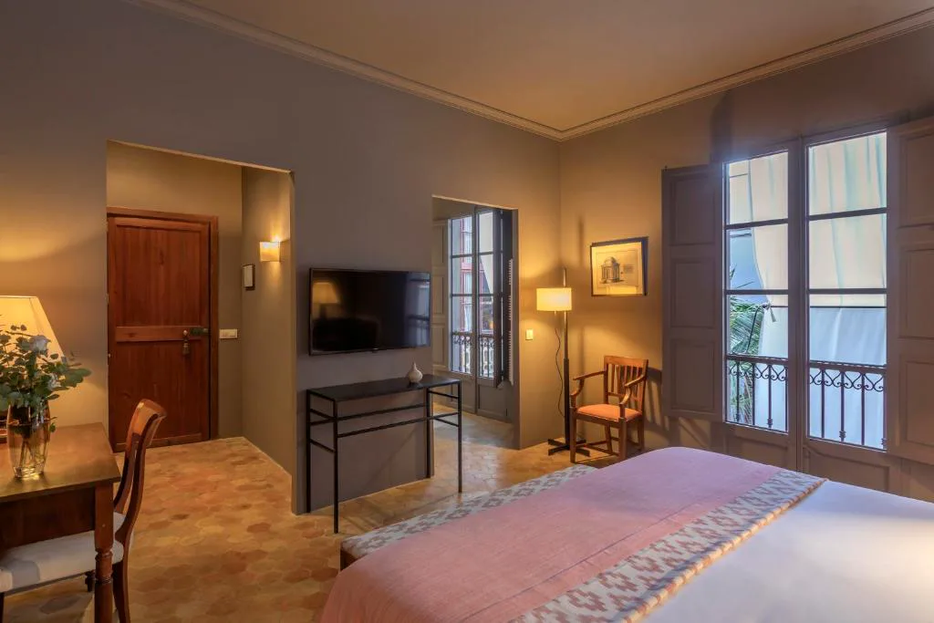 Dormitorio en tonos cálidos con balcón de forja abierto al casco antiguo, Can Cera Hotel