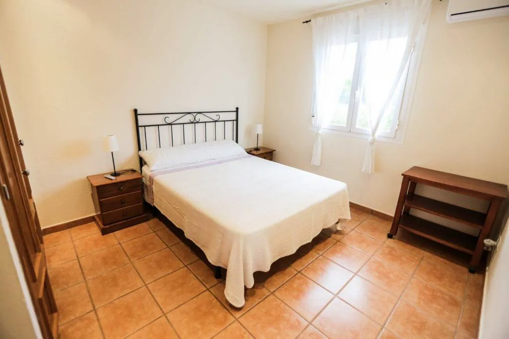 Dormitorio con cabecero de forja negra y cortinas blancas, Can Furnet