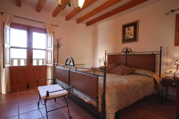 Dormitorio con techo de vigas de madera y puertas abiertas al balcón, Can Gat