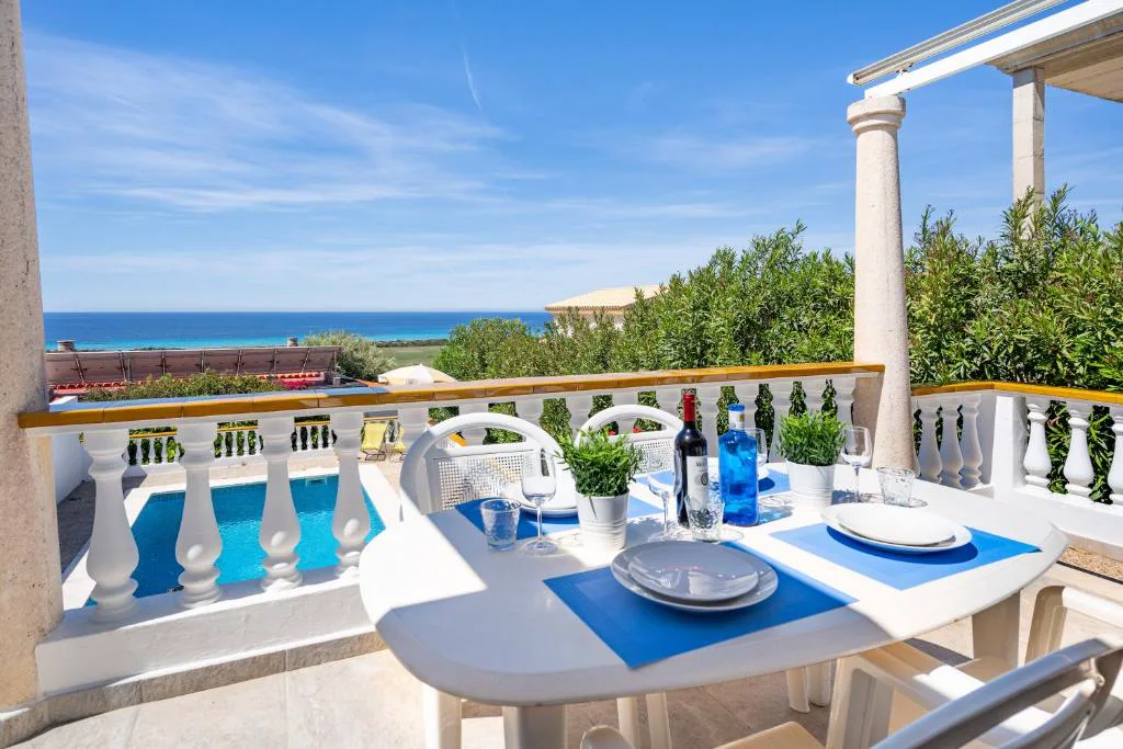 Terraza con mesa vestida en azul y vistas al mar entre columnas blancas, Can Poriol