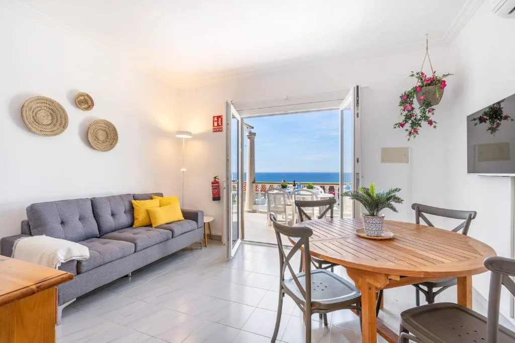 Salón luminoso con sofá gris y puertas abiertas al balcón con vistas al mar, Can Poriol
