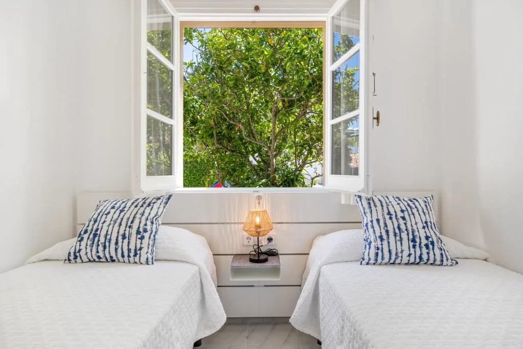 Dormitorio con dos camas individuales y ventana abierta a un limonero, Can Poriol