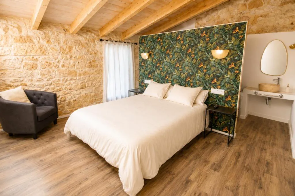 Dormitorio con pared de piedra vista y cabecero de estampado tropical, Can Roig