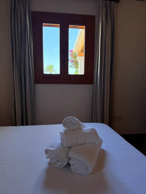 Dormitorio con toallas blancas enrolladas y ventana con vistas a una palmera, Can Vicent Sita
