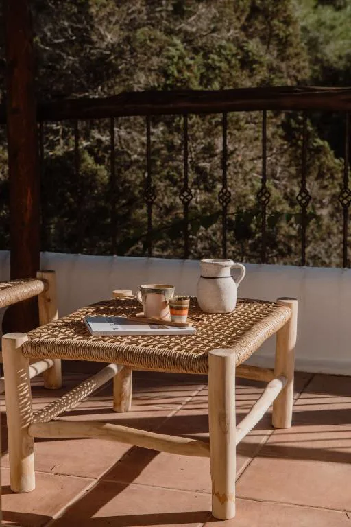 Mesa de fibra natural con jarra de cerámica en la terraza entre pinos, Can Vistabella