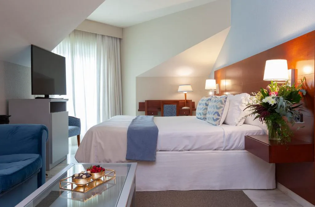 Habitación doble con sofá azul, cabecero de madera y ramo de flores frescas, Hotel Carlos I Silgar