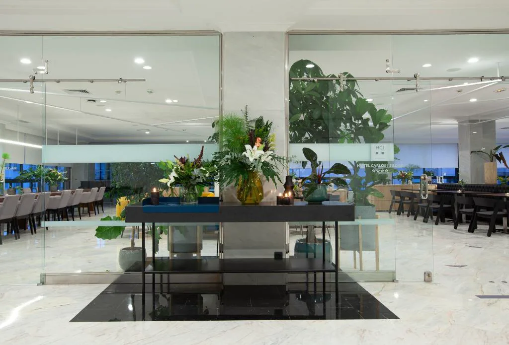 Recepción acristalada con ramos de flores y plantas junto a la cafetería, Hotel Carlos I Silgar