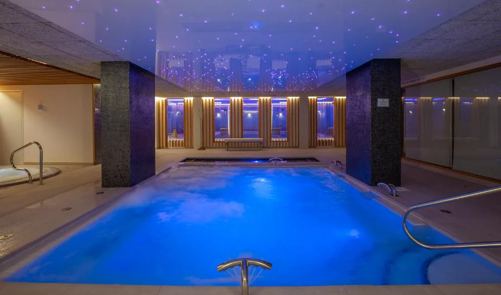 Piscina interior climatizada del spa con iluminación azul nocturna y zona de hidromasaje, Hotel Carlos I Silgar