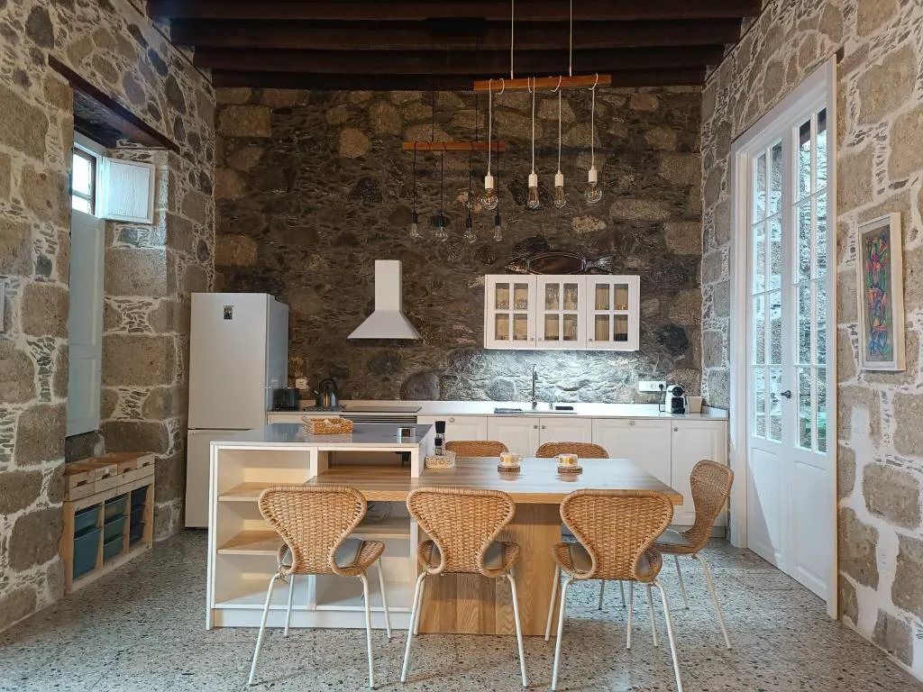 Cocina de piedra vista con instalación de bombillas colgantes y armarios blancos con cristaleras, Casa Bailarina