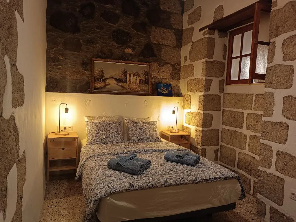 Dormitorio de piedra vista con cuadro antiguo y ropa de cama de estampado paisley, Casa Bailarina