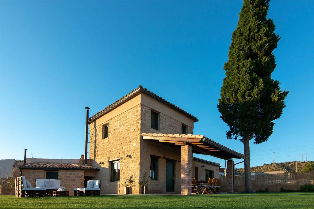 Casa de piedra y ladrillo con un ciprés