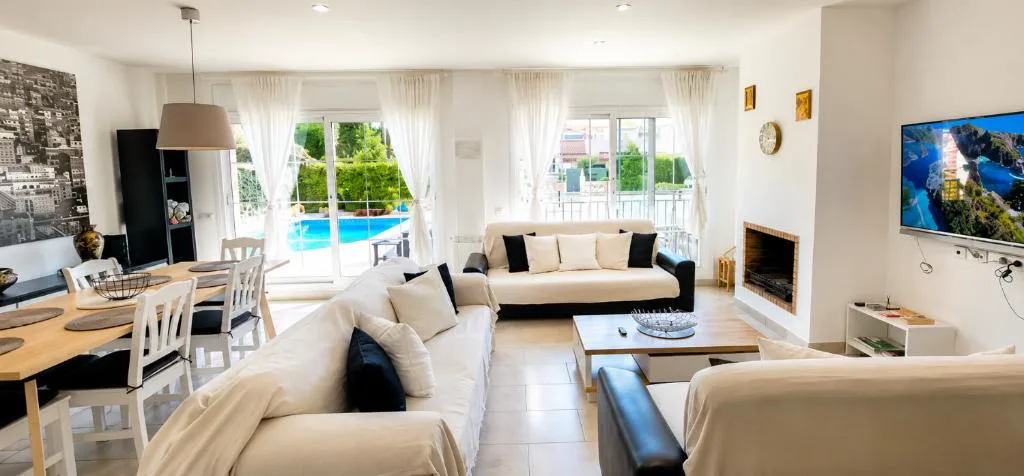 Salón blanco con sofás y ventanales a la piscina