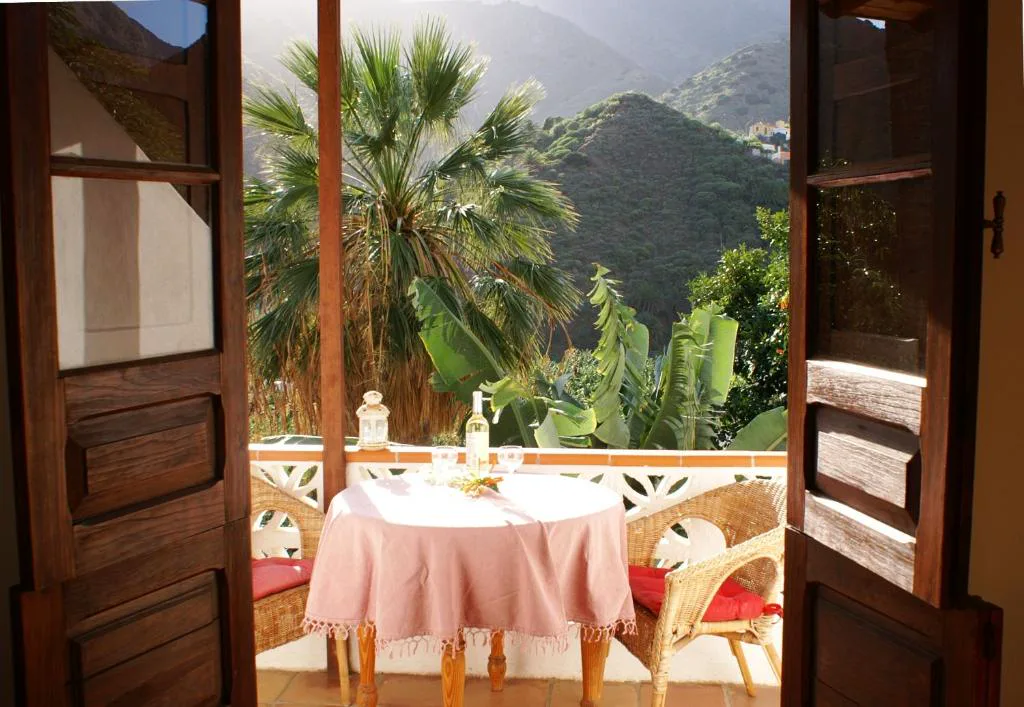 Terraza con mesa vestida de rosa y vistas a las montañas de Hermigua entre palmeras, Casa Creativa