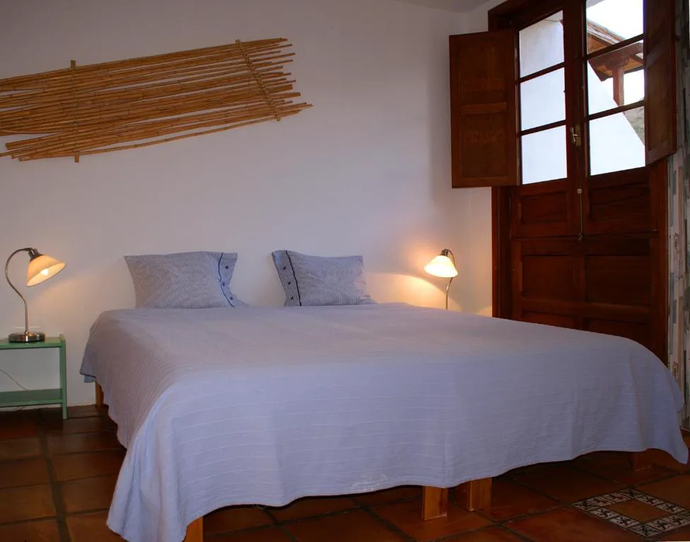 Dormitorio sencillo con cabecero de bambú y puerta de madera abierta al patio, Casa Creativa