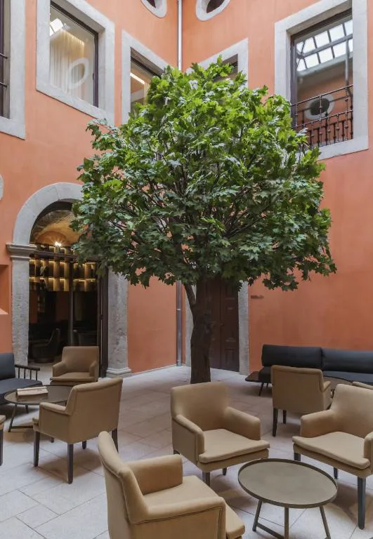 Patio interior con un árbol y sillones bajo la fachada en tono terracota, Casa da Companhia