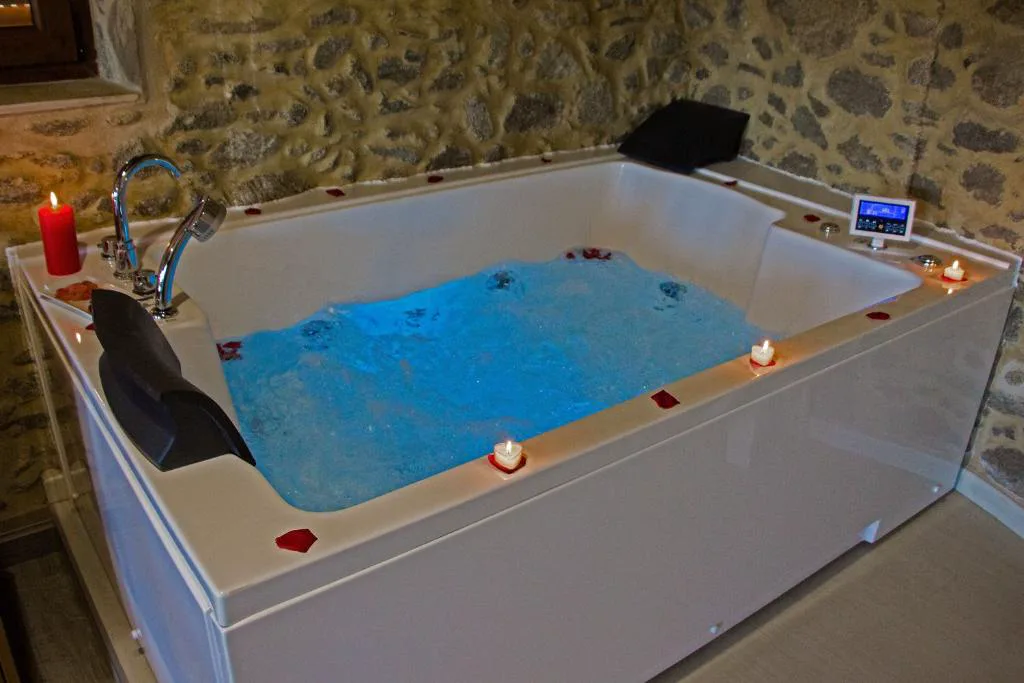 Bañera de hidromasaje con velas y pétalos de rosa junto a pared de piedra, Casa das Fiadeiras de Nemiña