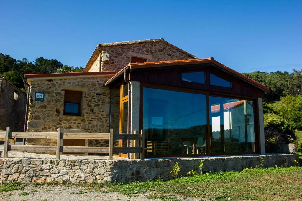 Fachada de piedra tradicional gallega con ampliación acristalada moderna, Casa das Fiadeiras de Nemiña