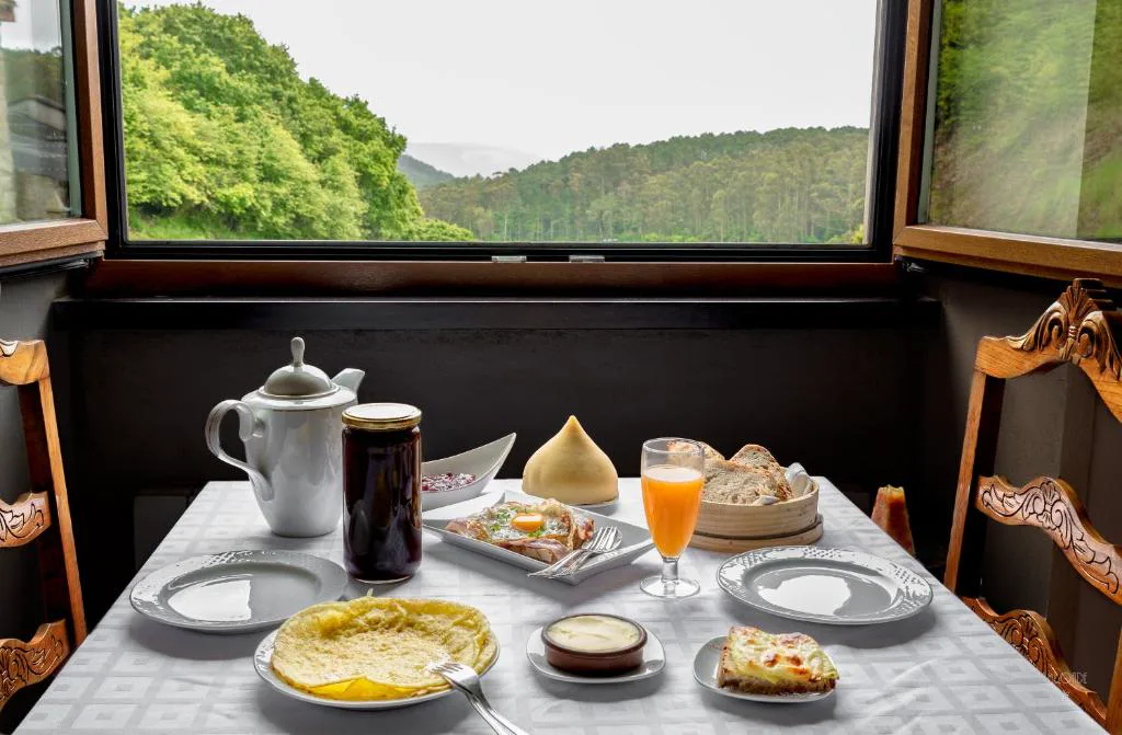 Mesa de desayuno junto a ventana abierta con vistas al valle, Casa das Fiadeiras de Nemiña