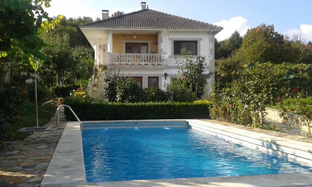 Piscina exterior con escalera junto a la fachada de la villa y jardín florido