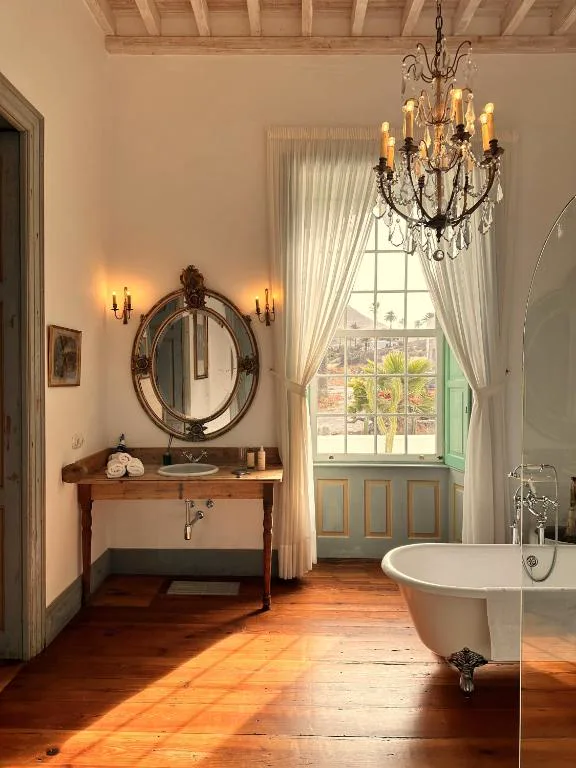 Baño de época con bañera de patas y espejo dorado bajo araña de cristal, Hotel Emblemático La Casa de los Naranjos