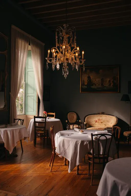 Comedor en tonos oscuros con araña de cristal y mesas vestidas de blanco, Hotel Emblemático La Casa de los Naranjos