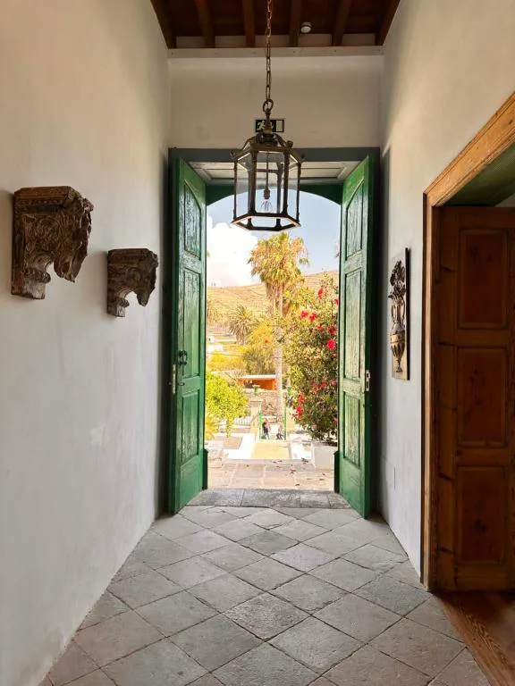 Pasillo con puertas verdes abiertas al jardín y candelabro de forja, Hotel Emblemático La Casa de los Naranjos