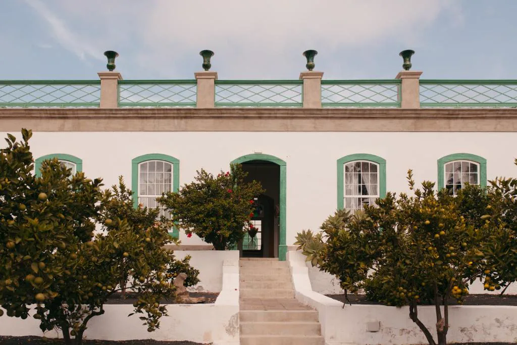 Fachada blanca con ventanas de arco verdes tras un jardín de naranjos, Hotel Emblemático La Casa de los Naranjos, Haría, Lanzarote