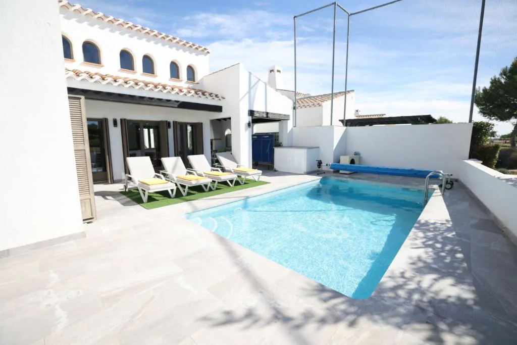 Piscina privada con tumbonas y sillones junto a la casa blanca