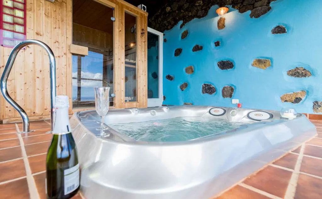 Jacuzzi con cabina de sauna de madera junto a una pared azul de piedra volcánica, Casa de Mi Abuela Maria
