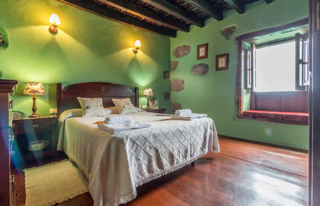 Dormitorio en tonos verdes con cabecero de madera tallada y piedra volcánica vista, Casa de Mi Abuela Maria