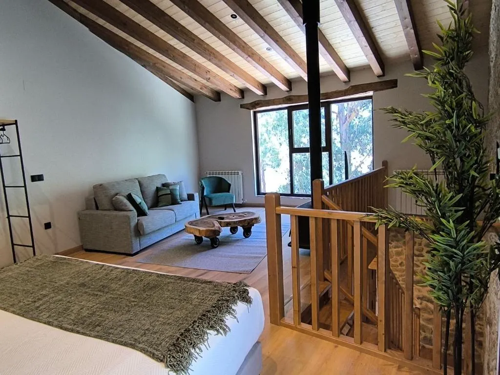 Altillo con cama, sofá y estufa de leña bajo techo de vigas de madera, en Casa Escondida Aveiga